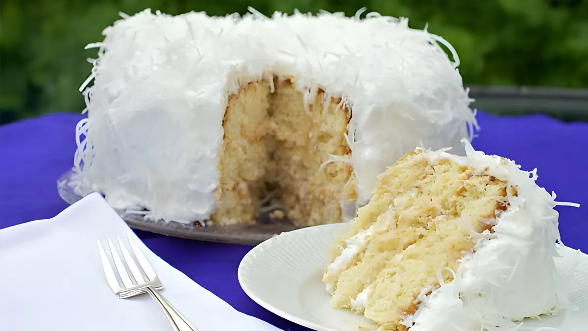 Slice of coconut cake served on a dessert plate with whipped cream, coconut cake recipe