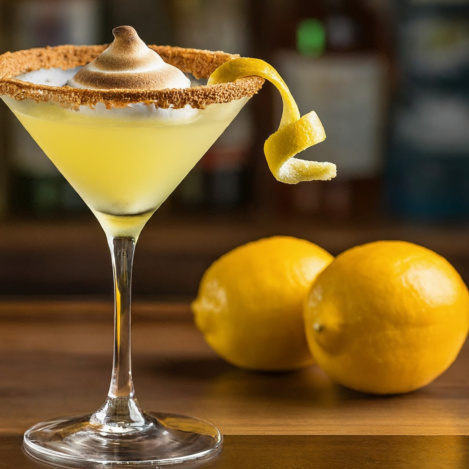 Lemon Meringue Martini with lemon peel and meringue garnish, graham cracker rim on wooden counter