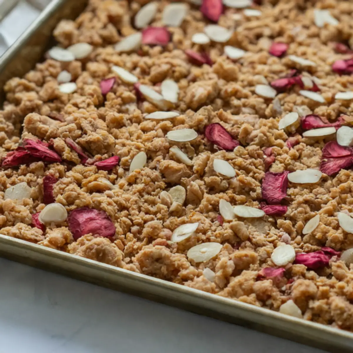 shot of a baking sheet filled with homemade strawberry crunch. The crumbly mixture is golden brown and studded with chopped dried strawberries and sliced almonds.