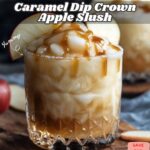 A tall glass filled with Caramel Dip Crown Apple Slush, the slushie is smooth and creamy with a rich caramel drizzle on top, garnished with a slice of green apple and set against a rustic wooden background with soft, warm lighting.